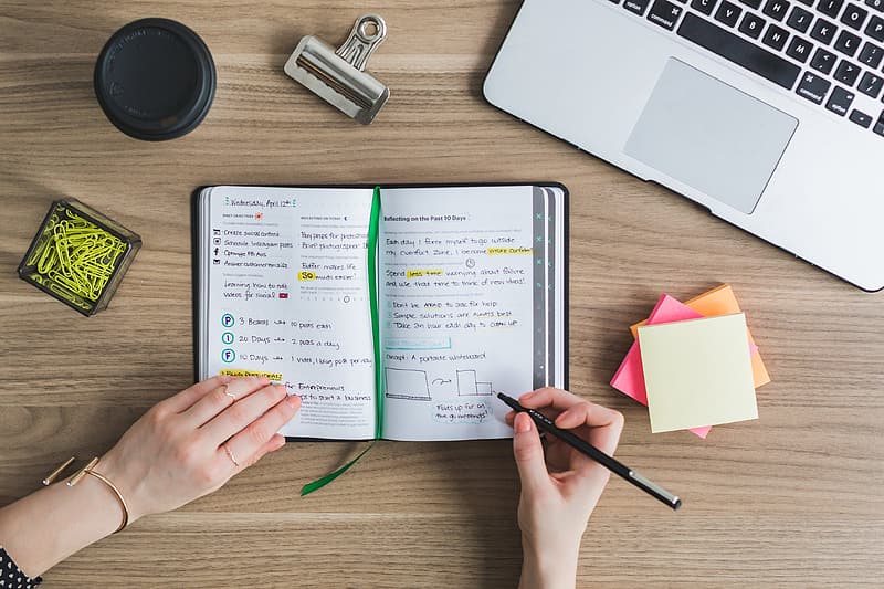 Woman writing on a planner beside silver macbook